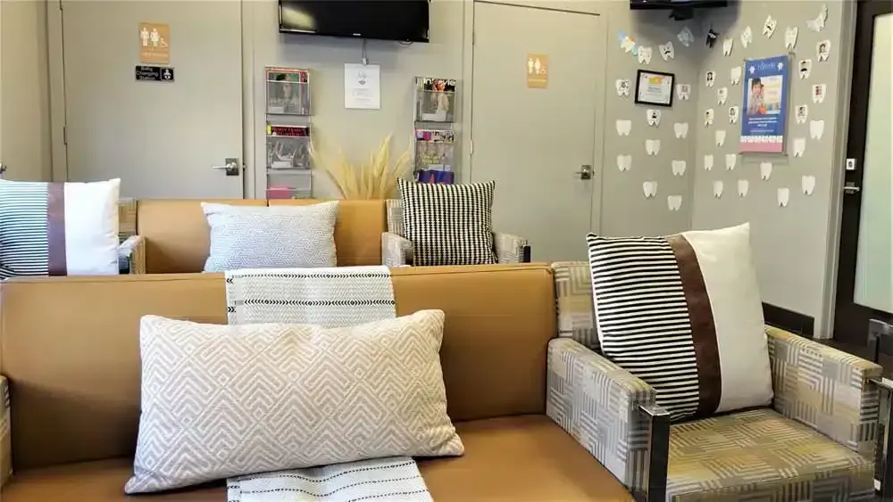 Waiting room with tan couches, patterned pillows, and a wall decorated with paper teeth.